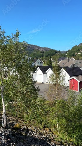 Vertical video. Residential houses in Norway, boat sailing in the river, view from railway embankment.