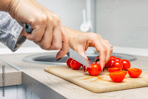 housewife cutting cherry tomato with knife on wooden board. woman's hand cutting cherry tomato with a knife. making tomato soup. cooking tomato salad. 