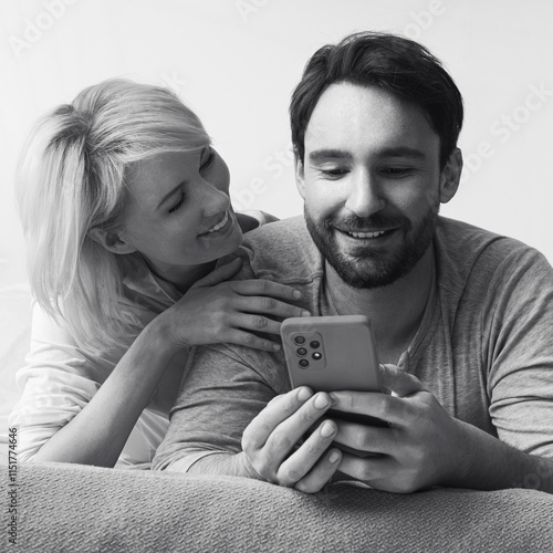 Monochrome bw image - couple lying on bed browsing internet reading text message use cellphone cell phone cellular device. Happy bearded man and woman shop online by smartphone. Technology. Square