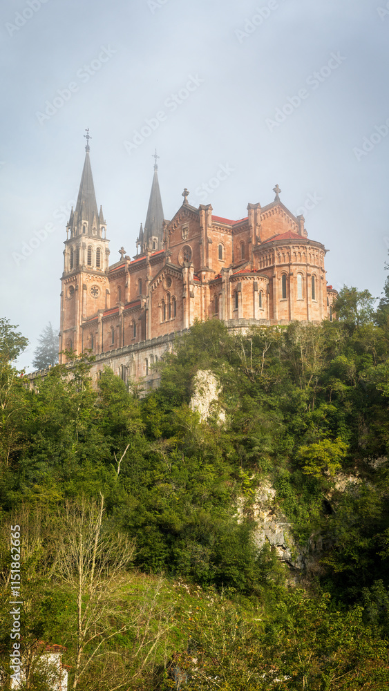 The stunning Basilica of Covadonga, perched on a hillside in the Picos de Europa mountains, enveloped by lush greenery and mist, is a symbol of Spanish religious heritage The stunning Basilica of Covadonga, perched on a hillside in the Picos de Europa mountains, enveloped by lush greenery and mist, is a symbol of Spanish religious heritage