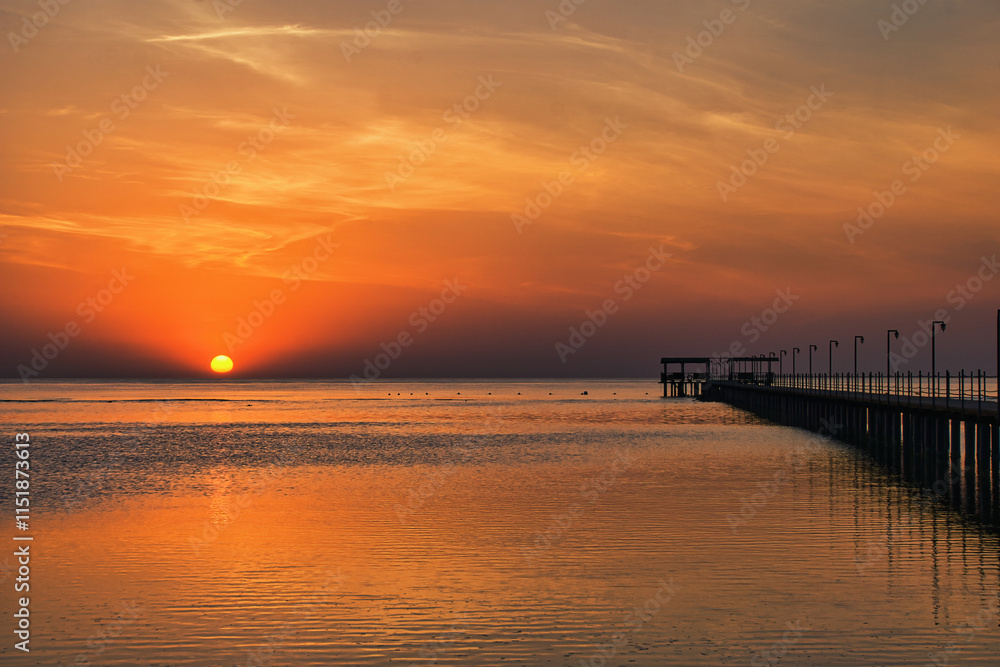 Beautiful sunrise on Red Sea, Marsa Alam, Egypt, outline of the boat, umbrellas, beach, chillout in the morning. Silhouettes of people against the background of sunrise, A jetty extending into the sea Beautiful sunrise on Red Sea, Marsa Alam, Egypt, outline of the boat, umbrellas, beach, chillout in the morning. Silhouettes of people against the background of sunrise, A jetty extending into the sea