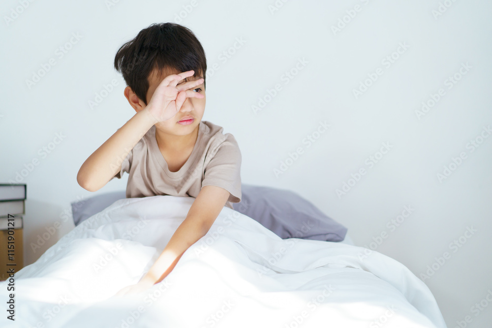 Asian boy wakes up in the early morning, feeling groggy and reluctant to leave the comfort of his bed. 