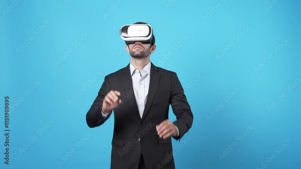 Businessman moving hand and managing data by using augmented reality technology. Caucasian investor wearing VR glasses and planning marketing strategy while standing at blue background. Apparatus. Businessman moving hand and managing data by using augmented reality technology. Caucasian investor wearing VR glasses and planning marketing strategy while standing at blue background. Apparatus.