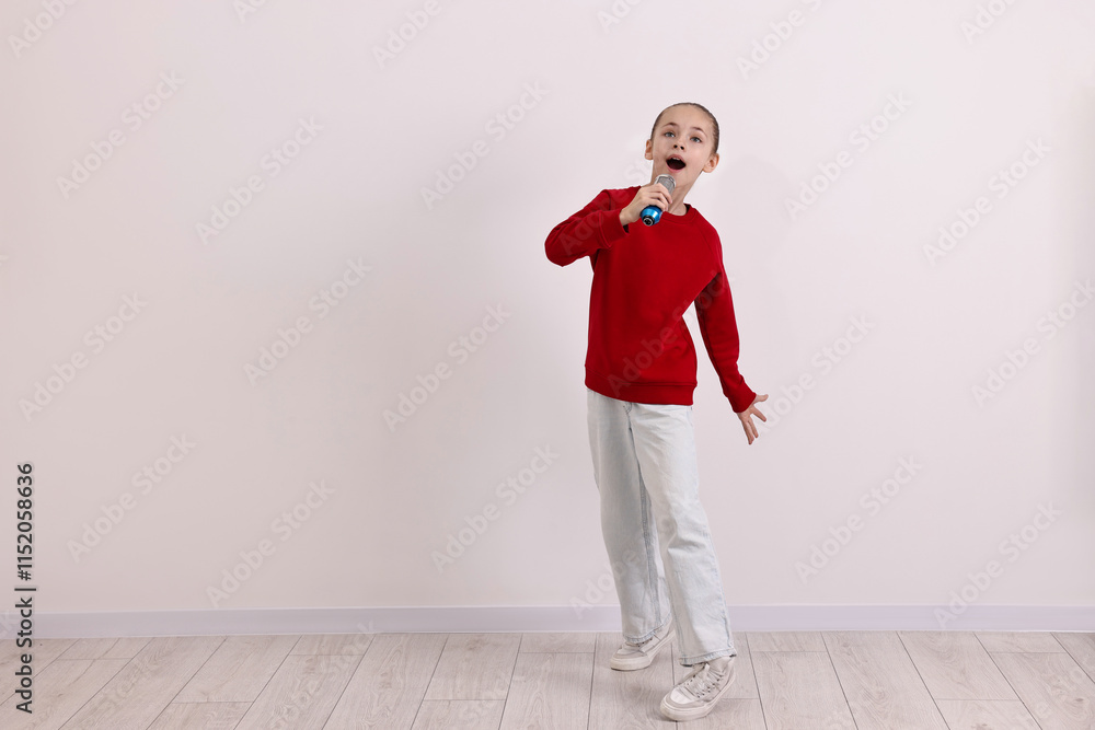 Little girl with microphone singing near white wall. Space for text Little girl with microphone singing near white wall. Space for text