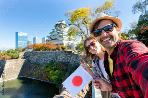 A young tourist couple taking a selfie with Japan flag at Osaka Castle, Osaka Castle is one of the most famous landmarks in Japan and Osaka, vacation lifestyle.