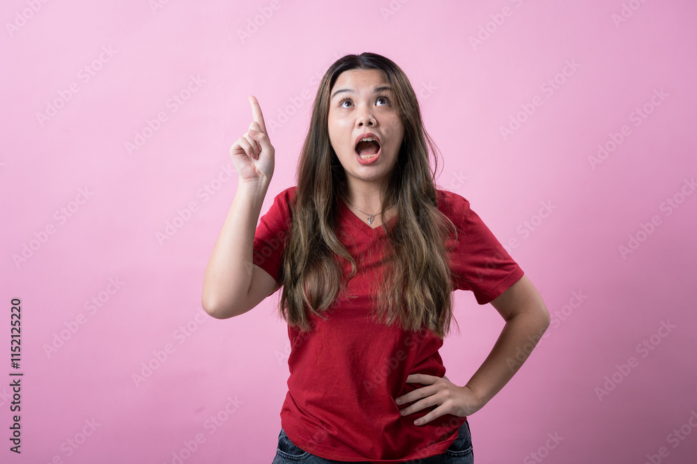 Asian woman in a red t-shirt and jeans standing against a pink background, smiling brightly with excitement, raising one finger upward as if having a new idea or solution Asian woman in a red t-shirt and jeans standing against a pink background, smiling brightly with excitement, raising one finger upward as if having a new idea or solution