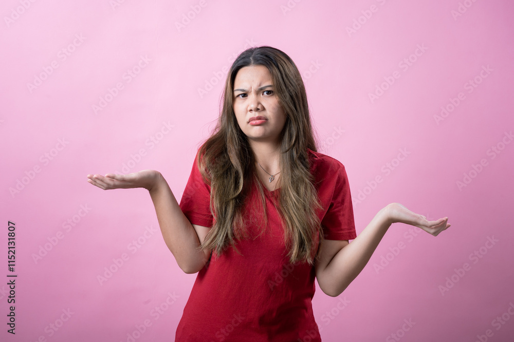 A confused young woman with long brown hair and light skin, wearing a red T-shirt, shrugs her shoulders and raises her palms with a puzzled facial expression against a solid pink background. A confused young woman with long brown hair and light skin, wearing a red T-shirt, shrugs her shoulders and raises her palms with a puzzled facial expression against a solid pink background.