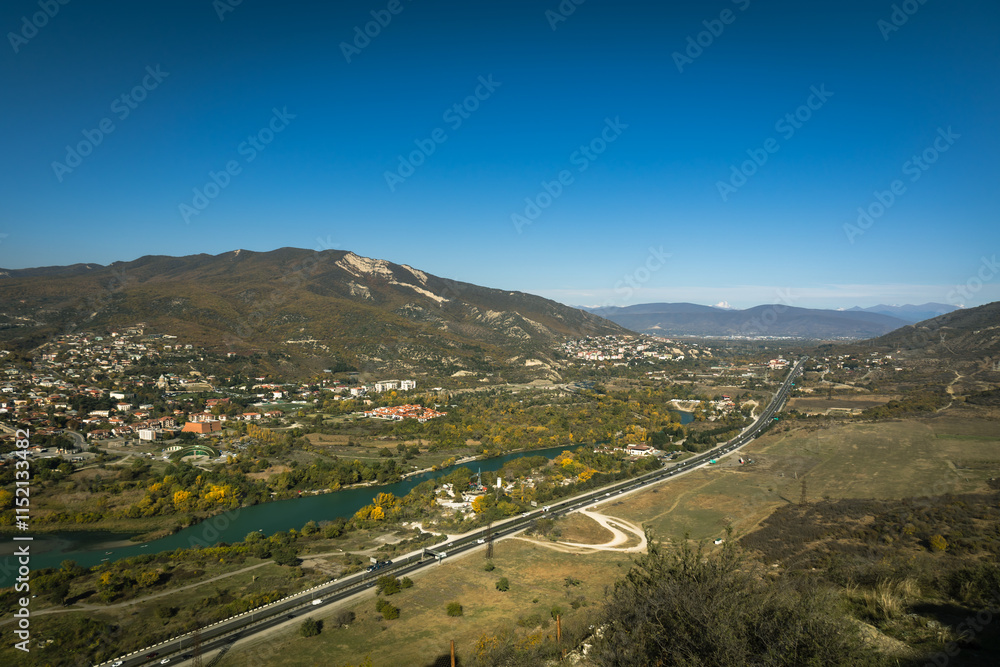 Fototapeta premium Autumn view from Jvari Monastery overlooking the historic town of Mtskheta and the Georgian Military Road. A scenic blend of cultural heritage and natural beauty under a crisp blue sky