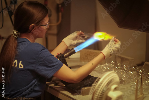 A young girl blows glass toys for the Christmas tree. Glass blower at a Christmas tree decorations factory. Fire and glass..
