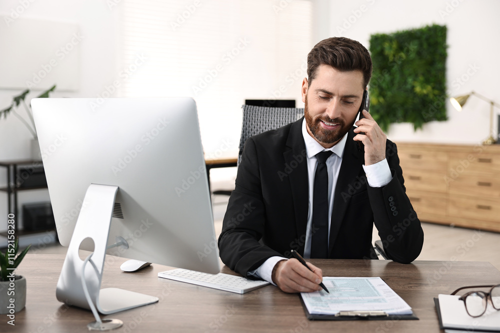 Man talking on smartphone while working at table in office Man talking on smartphone while working at table in office