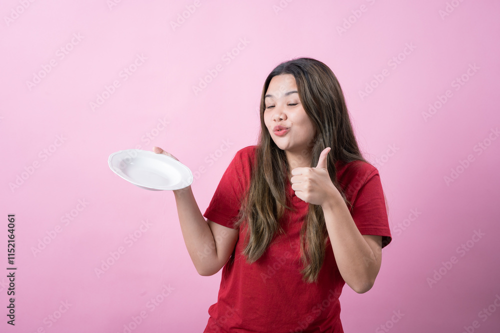 Excited young woman with long brown hair wearing a red t-shirt holding a white ceramic plate, presenting it with a surprised expression against a pink background. Excited young woman with long brown hair wearing a red t-shirt holding a white ceramic plate, presenting it with a surprised expression against a pink background.