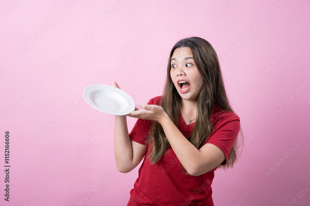 Excited young woman with long brown hair wearing a red t-shirt holding a white ceramic plate, presenting it with a surprised expression against a pink background. Excited young woman with long brown hair wearing a red t-shirt holding a white ceramic plate, presenting it with a surprised expression against a pink background.