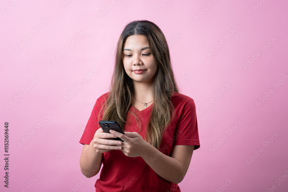 Surprised young woman with long brown hair wearing a red t-shirt looks at her smartphone against a pink background. Her shocked expression conveys excitement, disbelief, or unexpected news. Surprised young woman with long brown hair wearing a red t-shirt looks at her smartphone against a pink background. Her shocked expression conveys excitement, disbelief, or unexpected news.