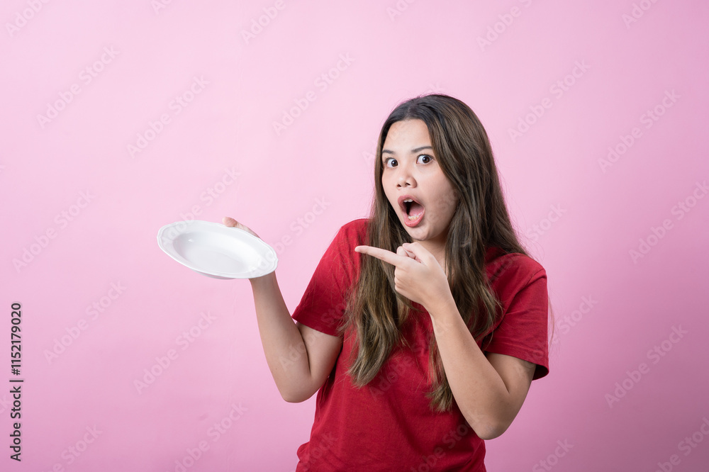 Excited young woman with long brown hair wearing a red t-shirt holding a white ceramic plate, presenting it with a surprised expression against a pink background. Excited young woman with long brown hair wearing a red t-shirt holding a white ceramic plate, presenting it with a surprised expression against a pink background.