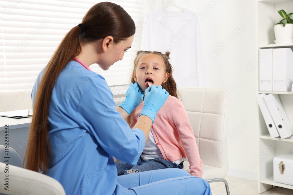 Obraz premium Doctor examining girl's throat with tongue depressor in clinic