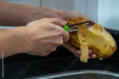 Potapo peeling. Hands peeling raw potato with vegetable peeler in the kitchen. photo