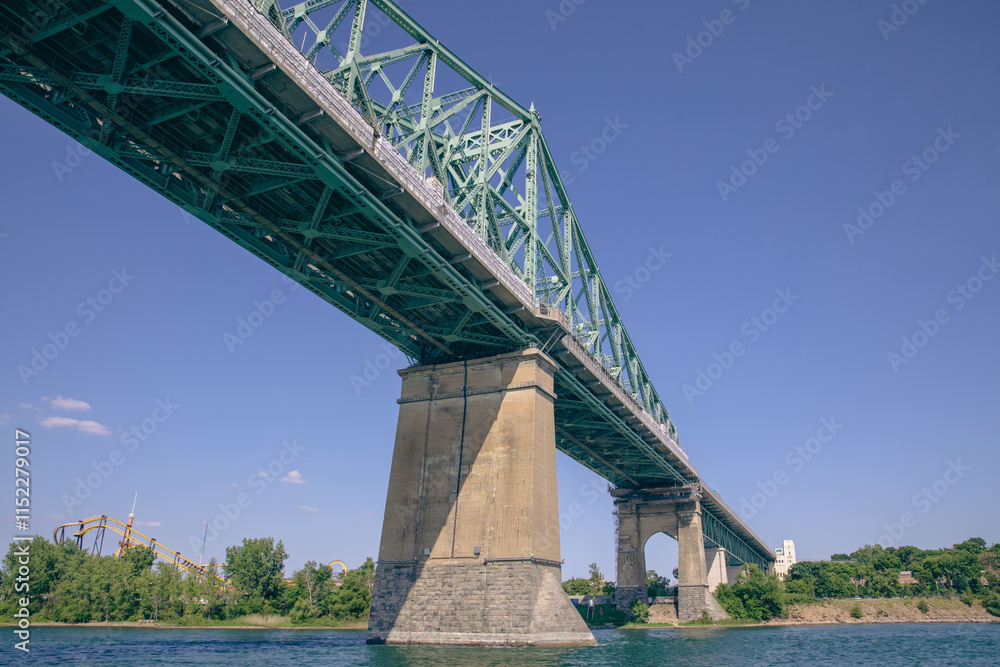 Fototapeta premium low point of view view of a green suspended bridge as seen from the river in summer