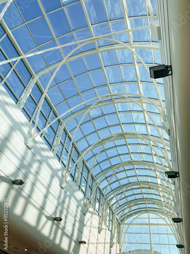 As I stand here, I find myself looking up at the beautifully designed glass roof of the building, marveling at the intricate details and symmetry of its frame and fixtures above me photo