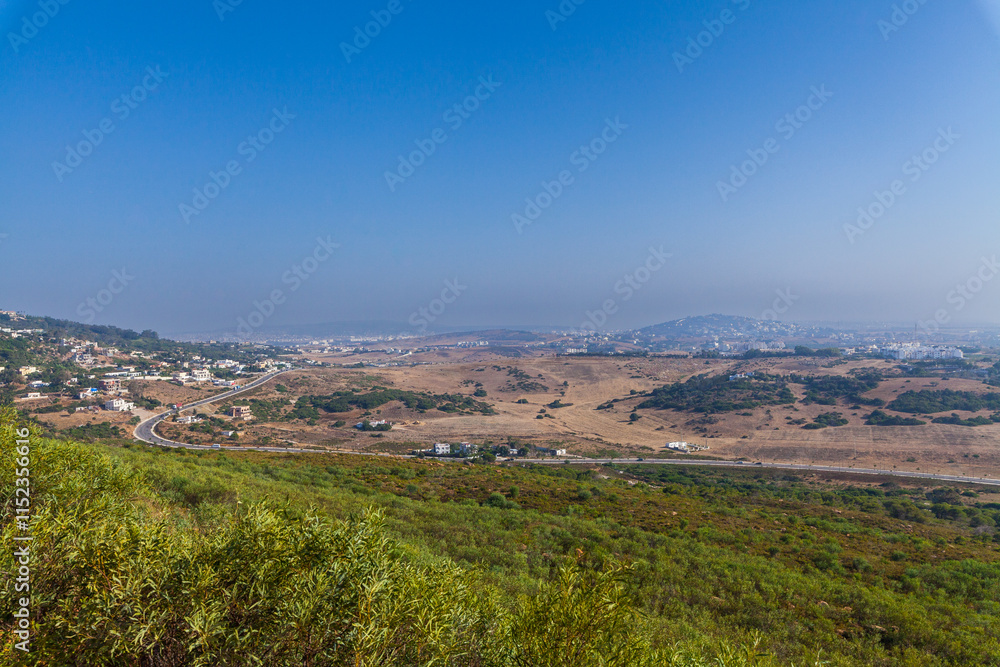 Naklejka premium breathtaking panoramic view of a coastal landscape, with rolling hills, a sprawling town, and a pristine coastline stretching towards the horizon, offering a serene and picturesque scene