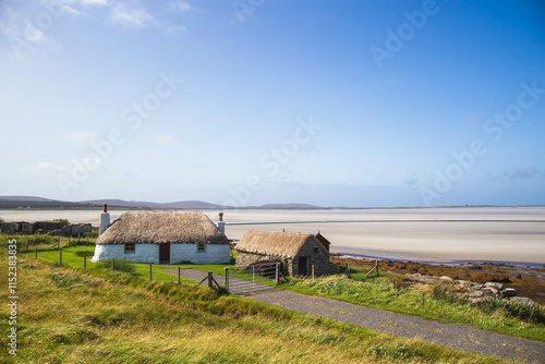 Traditionally white cottage with thatched roof, next to the turquoise bay.North Uist, Scotland photo