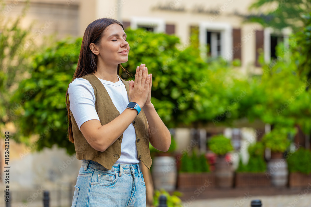 Young European woman praying with closed eyes to god asking for blessing, help, forgiveness outdoors. Pretty girl clasping hands wishing luck in sunny urban city street. Town religion lifestyles. Young European woman praying with closed eyes to god asking for blessing, help, forgiveness outdoors. Pretty girl clasping hands wishing luck in sunny urban city street. Town religion lifestyles.