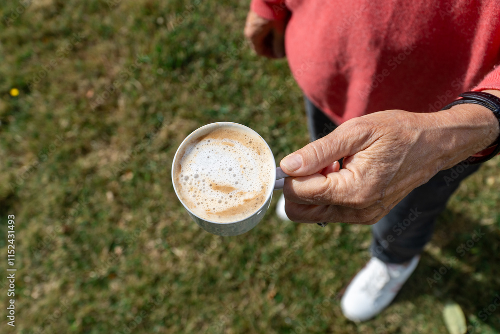 top view of a senior hand holding a cup of coffee while she is standing in the garden in a beautiful sunny day