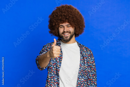 Like. Caucasian stylish man raises thumbs up agrees with something gives positive reply recommends advertisement likes good idea feedback celebrating success victory. Guy isolated on blue background photo