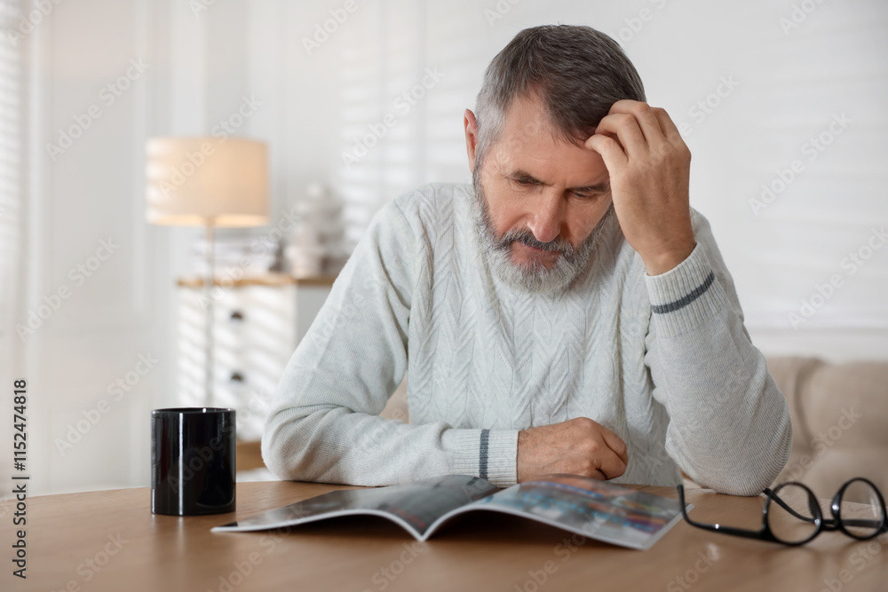 Senior man reading magazine at table indoors Senior man reading magazine at table indoors