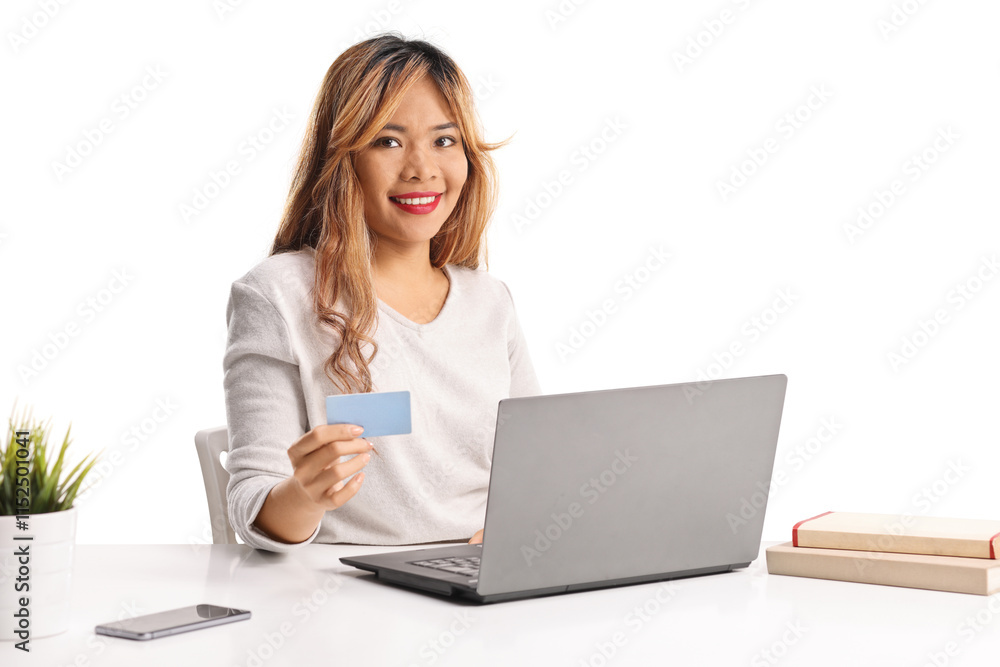 Asian woman holding a credit card and sitting at a desk with a laptop computer Asian woman holding a credit card and sitting at a desk with a laptop computer