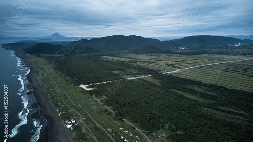 Aerial view of Khalaktyrsky Beach. A tranquil scene with a black sand beach, gentle waves, and lush mountains under a cloudy sky for a perfect getaway photo