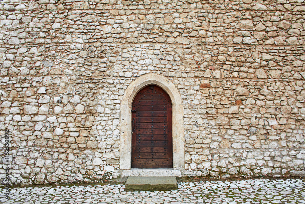 A small old wooden door with metal details in the stone wall of an ancient building. A small old wooden door with metal details in the stone wall of an ancient building.