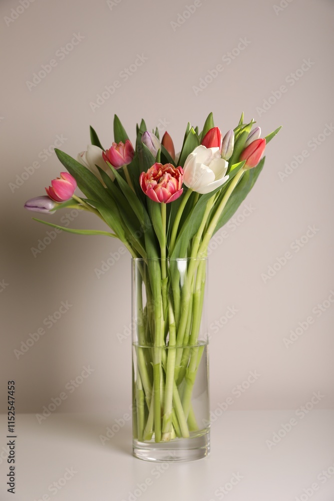Beautiful bouquet of colorful tulips in glass vase on beige background Beautiful bouquet of colorful tulips in glass vase on beige background