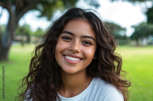 Portrait of a happy Latin American young girl with curly hair, smiling and playing in the park, with a green background.