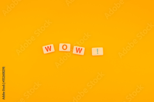 Scrabble tiles spelling WOW on vibrant yellow background