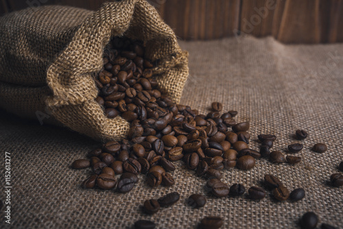 Burlap sack spilling roasted coffee beans on a rustic burlap surface photo