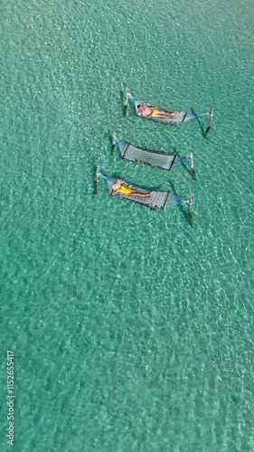 Experience the tranquility of Koh Kood Island, where relaxation is found lounging on hammocks over clear turquoise waters, A diverse couple of men and women on vacation or honeymoon in Thailand photo