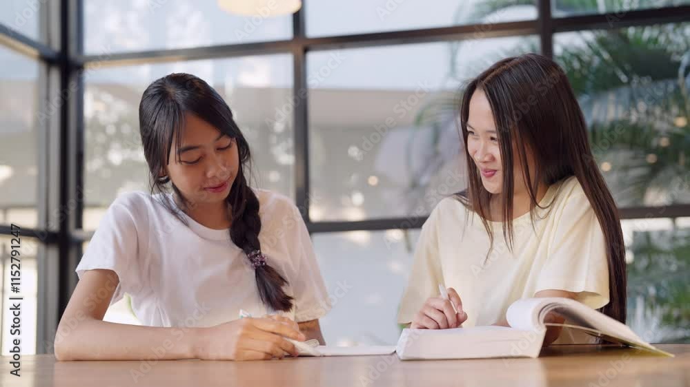 Two women sitting at a table with books and writing. One of them is wearing a white shirt Two women sitting at a table with books and writing. One of them is wearing a white shirt