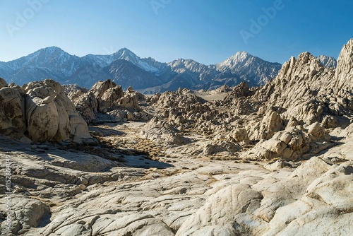 High-resolution landscape image featuring a striking mountain range beneath a clear blue sky, emphasizing jagged peaks and rocky terrain with contrasting shadows and sunlight. photo