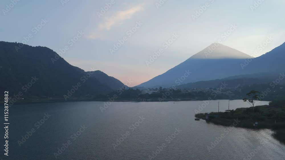 Tranquil lake scene at sunset with a silhouette of a volcano and surrounding hills, showcasing natural beauty in Guatemala