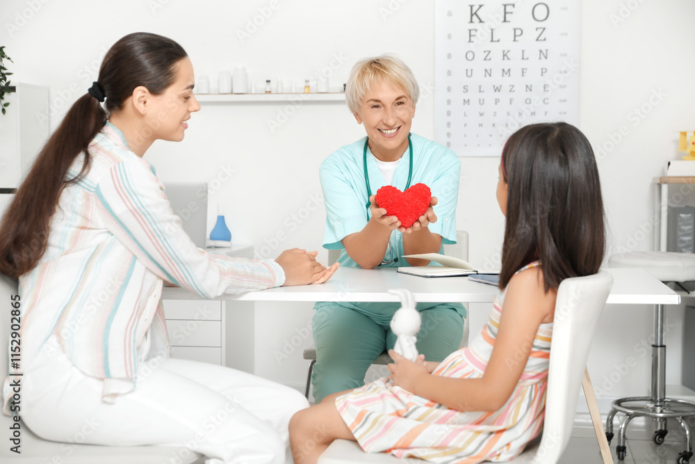 Female pediatrician giving toy heart to little girl and mother in clinic Female pediatrician giving toy heart to little girl and mother in clinic