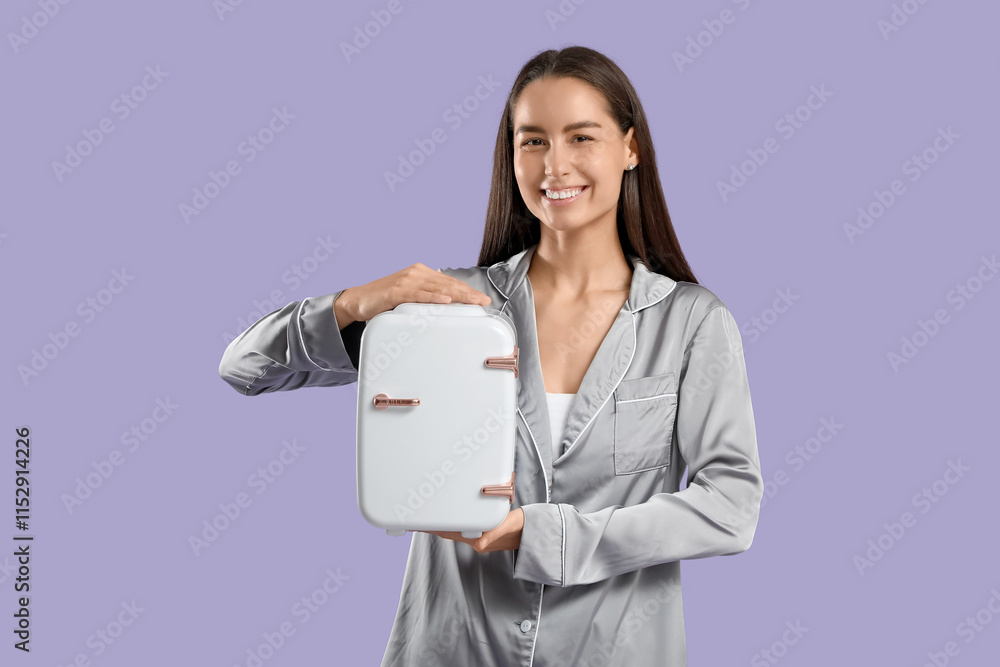 Happy young woman with small cosmetic refrigerator on purple background Happy young woman with small cosmetic refrigerator on purple background