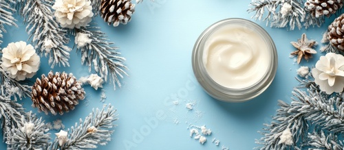 Winter skincare essentials featuring natural cosmetics with cream in a glass jar surrounded by pinecones and frosted foliage on blue backdrop photo