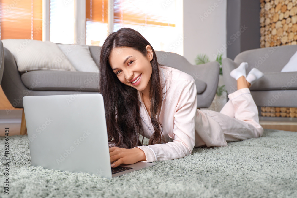 Female freelancer in pink pajamas working with laptop on carpet at home Female freelancer in pink pajamas working with laptop on carpet at home