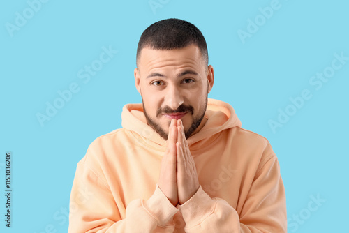 Apologetic young man on blue background, closeup photo