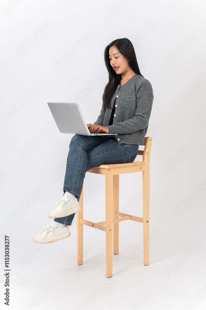 A beautiful Asian woman sits on a chair on a white studio background, working on her laptop. A beautiful Asian woman sits on a chair on a white studio background, working on her laptop.