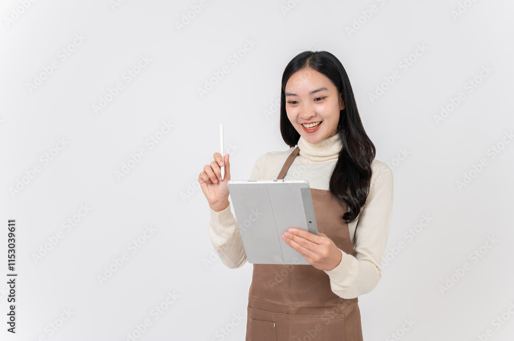 A smiling female waitress or coffee shop staff in a brown apron writes order in her digital tablet. A smiling female waitress or coffee shop staff in a brown apron writes order in her digital tablet.
