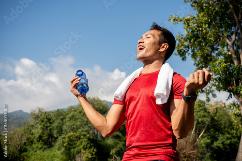 Happy Asian man in sportswear feels refreshed after drinking water following his workout in a park. photo