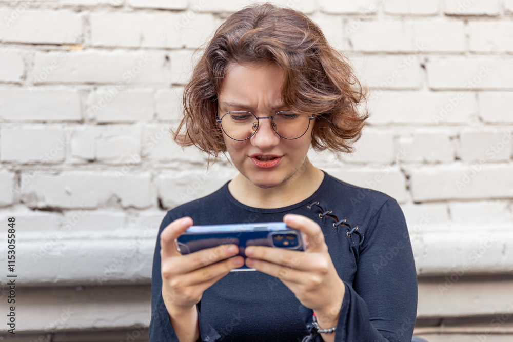 Fototapeta premium Young female gamer playing games on the phone in a cafe. Emotions concept.