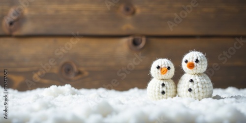A pair of charming handcrafted snowmen, crafted from fluffy yarn, stand nestled in a soft, pristine blanket of artificial snow, set against a rustic wooden backdrop.