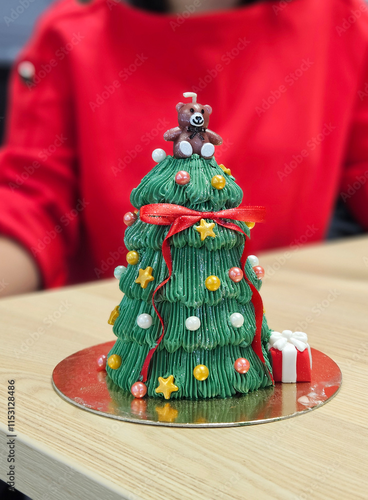 Green color Christmas tree shape cake and red color ribbon bow with teddy bear candle
